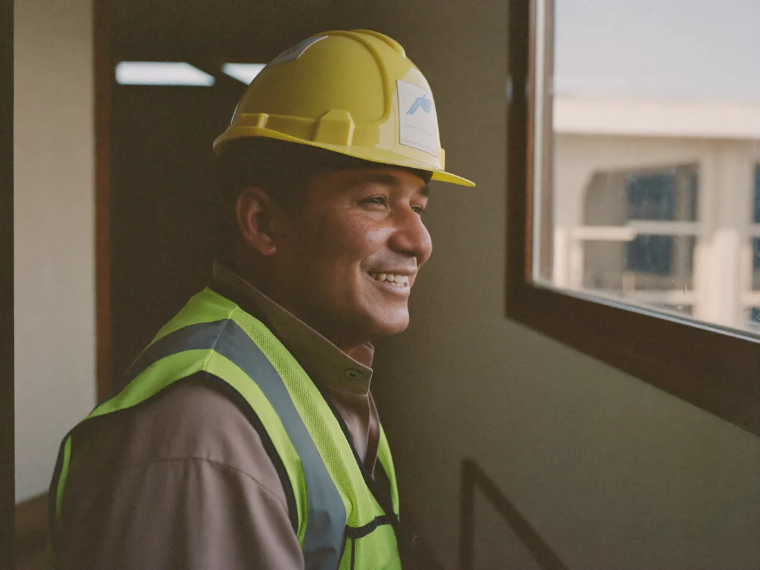 Trabajador de obra con casco y chaleco, sonriendo