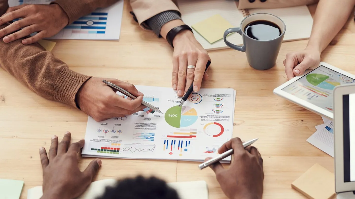 Imagen ilustrativa. Personas revisan gráficos sobre una mesa de reunión.